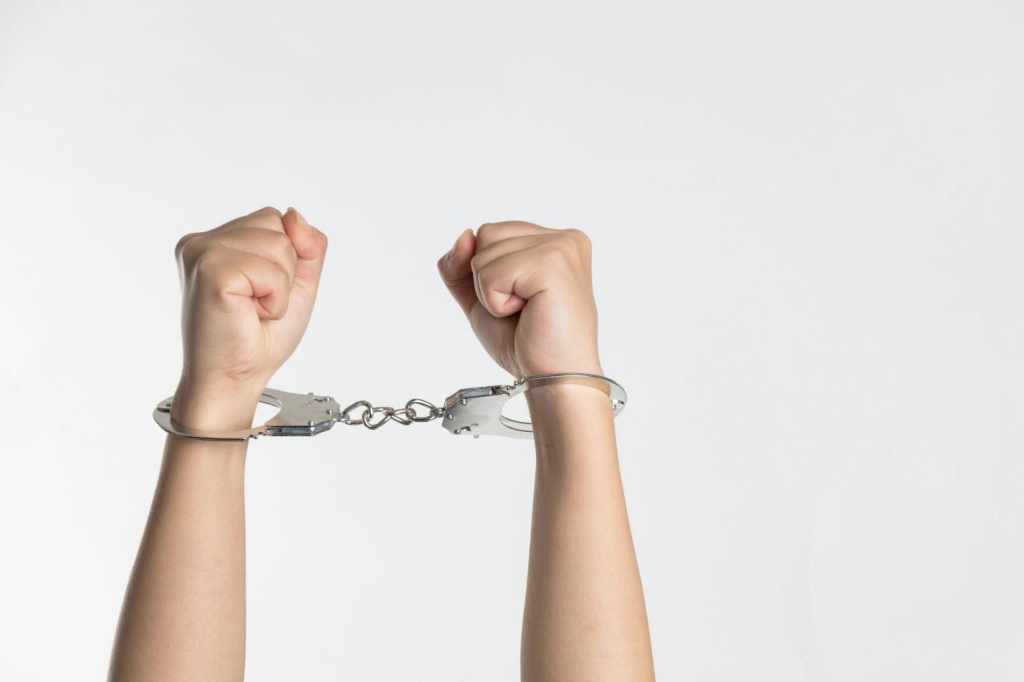 Image of hands in silver handcuffs with a plain white background.