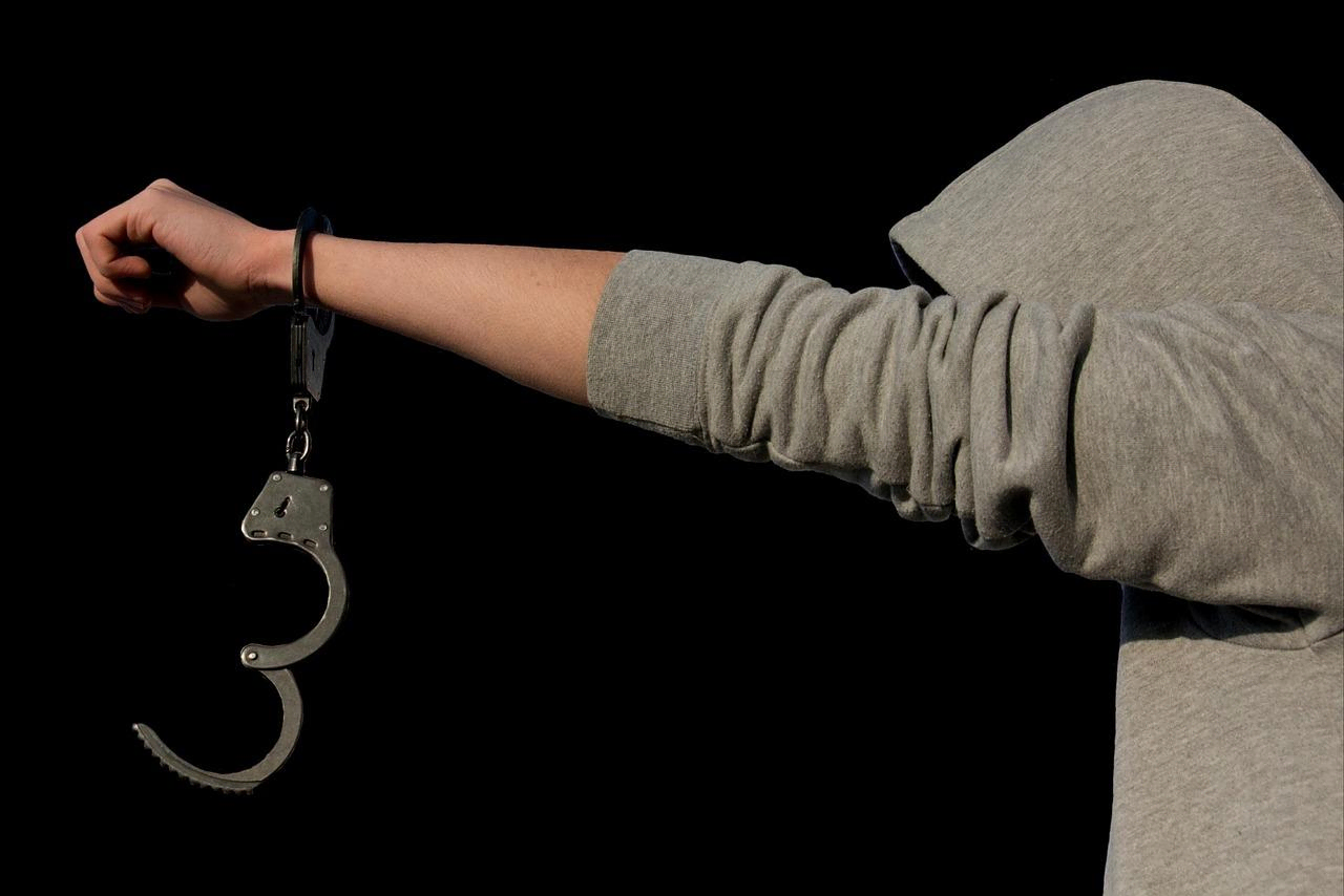 Hands in handcuffs against a dark black background.