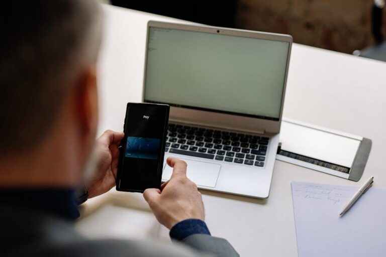 Businessman using a smartphone for digital payment beside a laptop representing technology in the bail process in North Carolina
